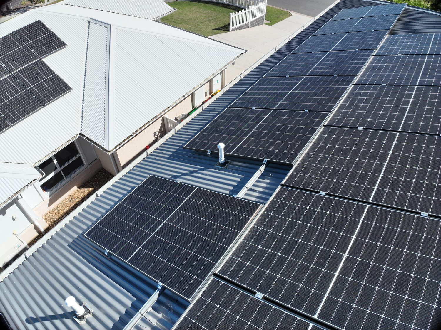 Wide context frame of a plumbing vent penetration on a metal roof beside a rooftop solar array
